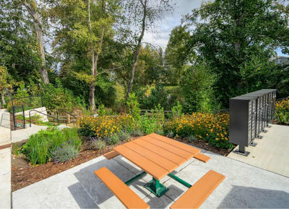 A wooden picnic table with green benches is surrounded by a concrete patio and a fence.