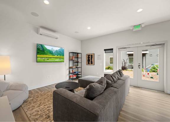 A living room with a grey couch and a painting of a green landscape on the wall.