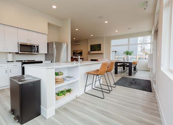 A kitchen with white cabinets and a black trash can.