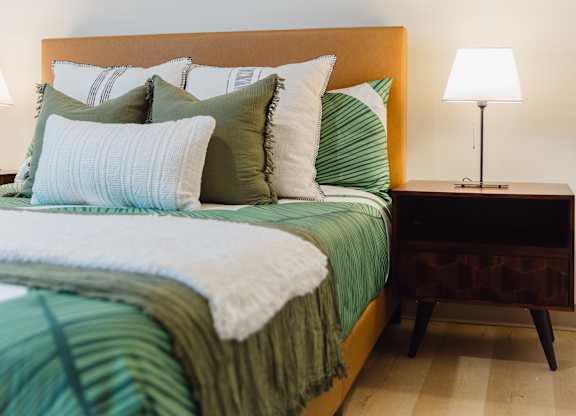 A bed with green and white bedding and a lamp on a side table.