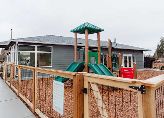 A playground with a green slide and a wooden fence.
