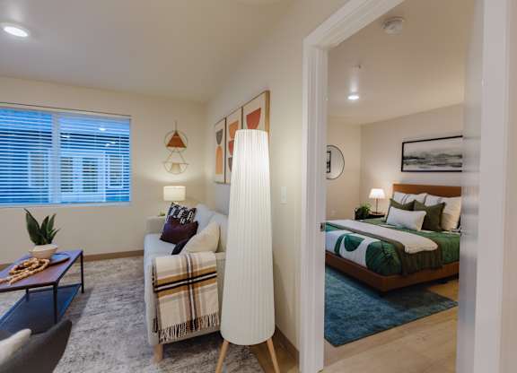 A well-lit bedroom with a bed, couch, and a table with a plant on it.
