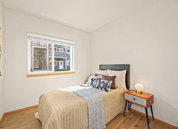 A bedroom with a bed, nightstand, and a window showing a view of a house.