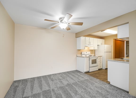 an empty living room with a kitchen and a ceiling fan