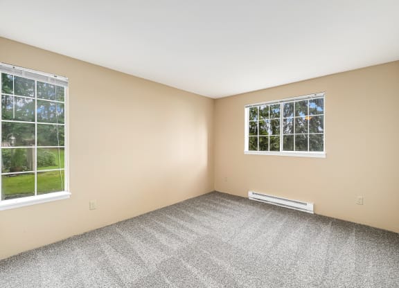 an empty room with two windows and carpeting