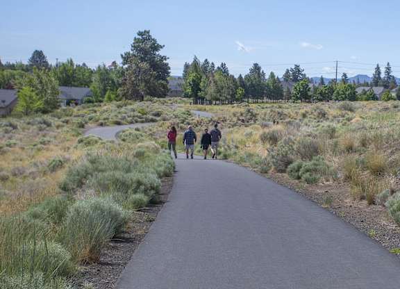 Three people walking on a paved trail through a grassy area.