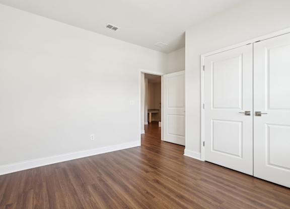 A room with white walls and wooden floors with a white door on the right.
