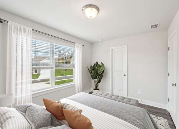 A bedroom with a large bed and a window with white curtains.