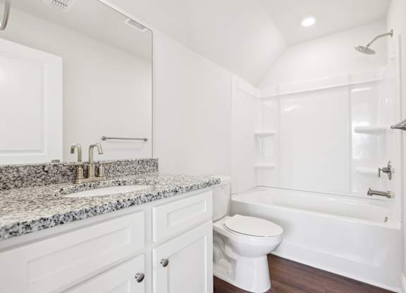 A white bathroom with a granite countertop and a white bathtub.