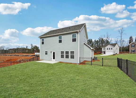 A house with a grey roof and white walls is surrounded by a black fence.