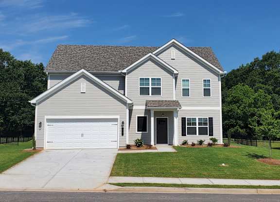 A two-story house with a garage is surrounded by a green lawn and trees.