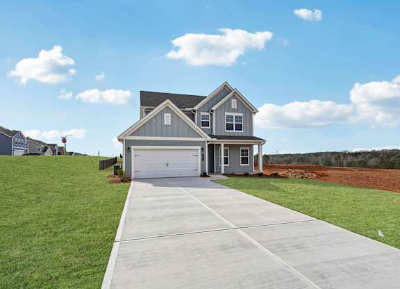 A house with a grey roof and a garage door is in front of a grassy area.