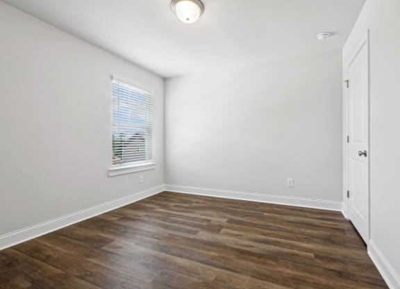 an empty room with white walls and wood flooring and a window