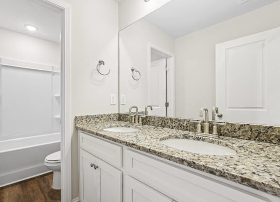 a bathroom with white cabinets and granite counter tops and a sink and a toilet