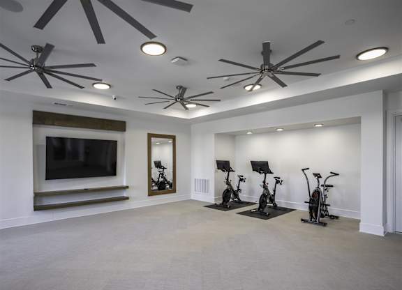 A spacious room with a ceiling fan, exercise bikes, and a television.