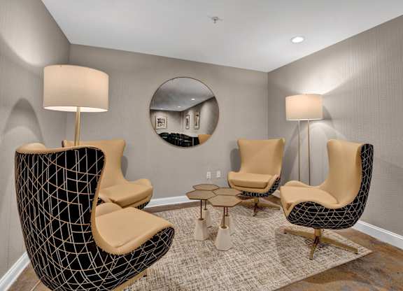 A living room with a black chair and a round mirror on the wall.