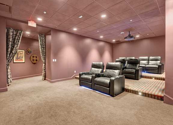 A home theater room with a carpeted floor and a row of black leather chairs.