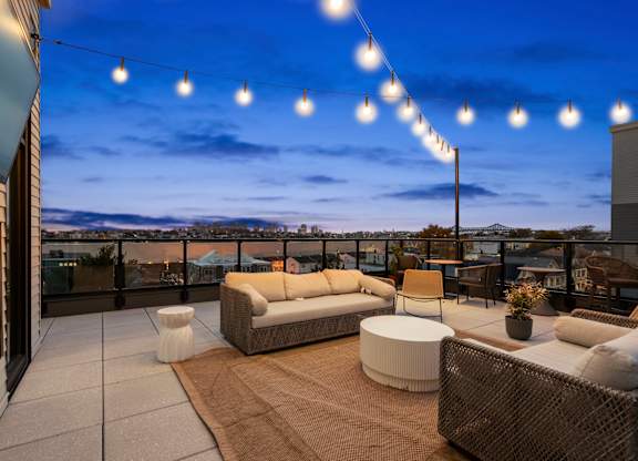 A patio with a couch, chairs, and a table with a view of the city.