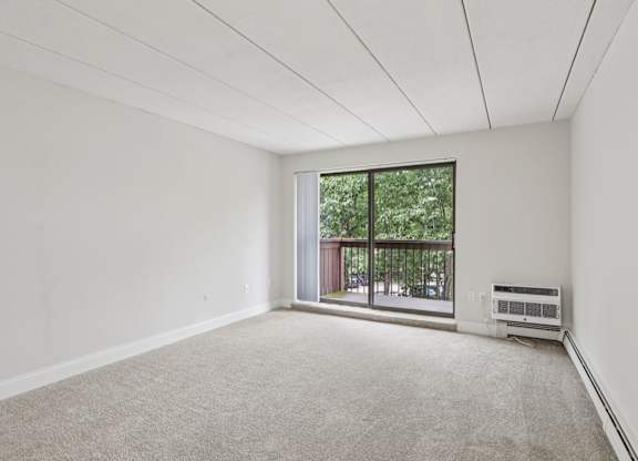A room with a carpet floor and a window with a view of a balcony.