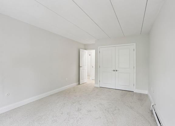 A room with white walls and carpeted floor with two doors.