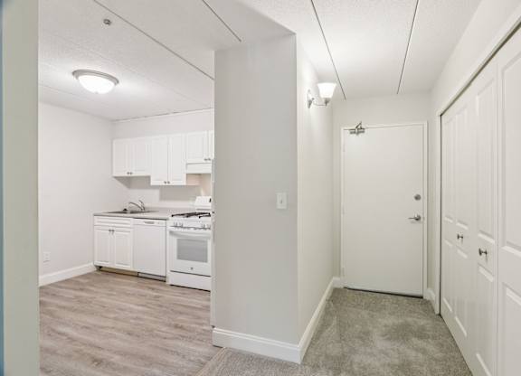 A kitchen with white cabinets and appliances in a room with a carpeted floor.