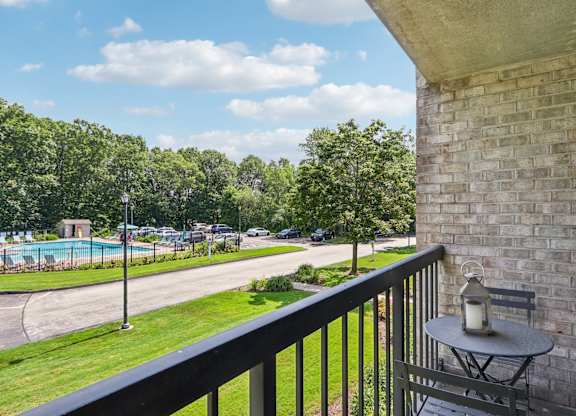 A balcony with a table and a lantern overlooking a pool and trees.