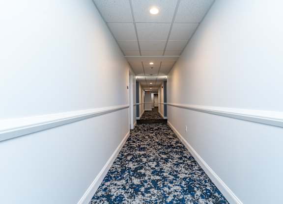 a long corridor with white walls and blue carpet
