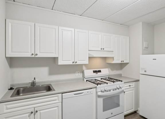 A white kitchen with a stove, sink, and cabinets.