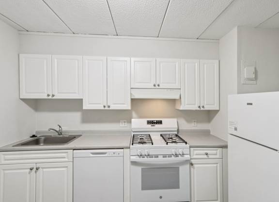 A white kitchen with a stove, sink, and refrigerator.