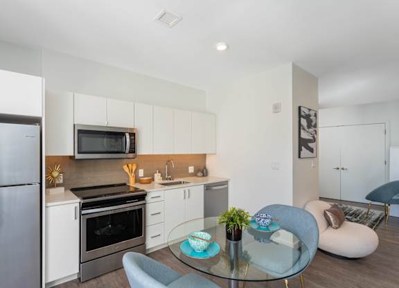 A modern kitchen with a glass table and grey chairs.