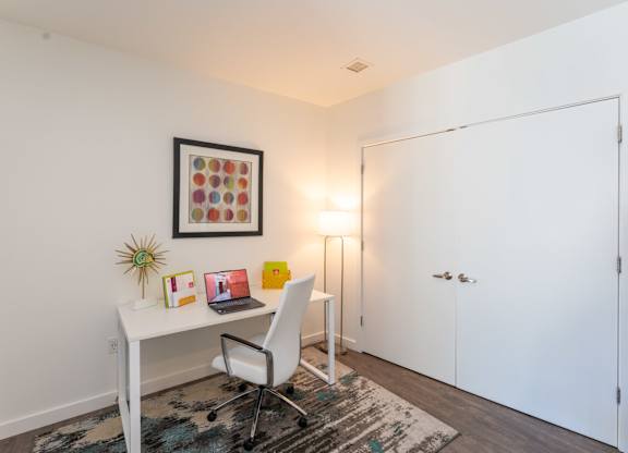 A white desk with a chair and a picture frame on the wall.