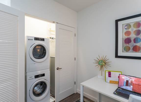 A small room with a washing machine and a laptop on a desk.