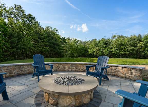 A stone fire pit sits in the middle of a patio with blue chairs on either side.