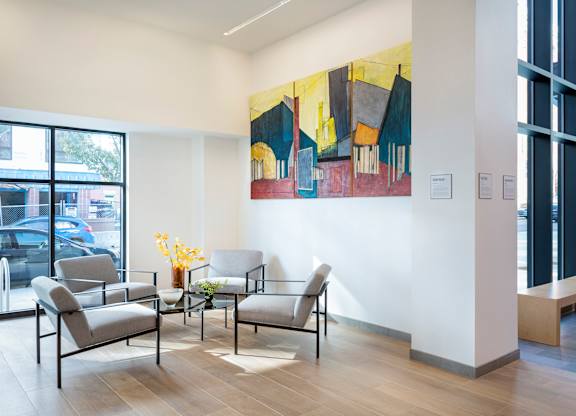 A large painting hangs on the wall above a table with chairs in a room with a window.