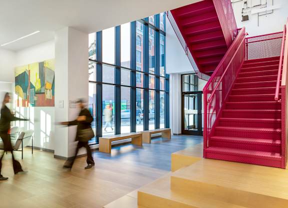 A red staircase in a modern building with people walking in the background.