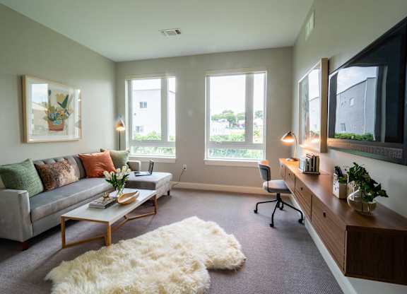 A bedroom setup with a desk area featuring large windows that allow natural light to brighten the room.