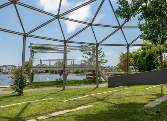A serene waterfront scene at PORT Park with a bench and a view of the river and a distant bridge, offering a relaxing spot in the neighborhood.