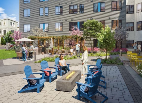 A vibrant courtyard in the DUO apartment complex, designed with paved walkways and lush landscaping. The area includes blue Adirondack chairs arranged around a modern fire pit, with residents engaging in conversations. Additional seating areas with tables and umbrellas are visible, surrounded by flowering trees and well-maintained greenery, creating a communal and inviting outdoor space.