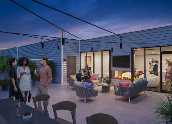 A sophisticated roof deck at dusk, featuring comfortable outdoor seating with sofas and armchairs around a central fire pit. Ambient string lights and modern lighting fixtures enhance the cozy atmosphere. Residents are seen enjoying the space, engaging in conversations against the backdrop of a twilight sky, making it ideal for evening gatherings.