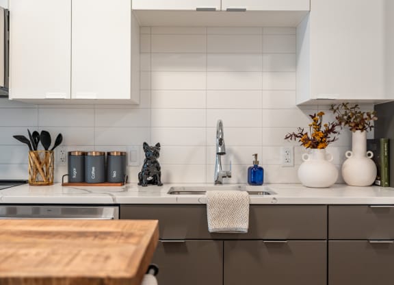 a white kitchen with gray cabinets and a black cat on the counter