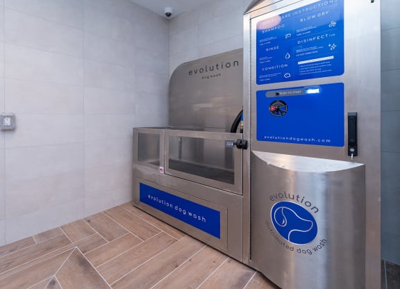 Evolution dog wash station at DUO Apartments with a stainless steel tub, detailed instructions on the care screen, and modern tiled walls