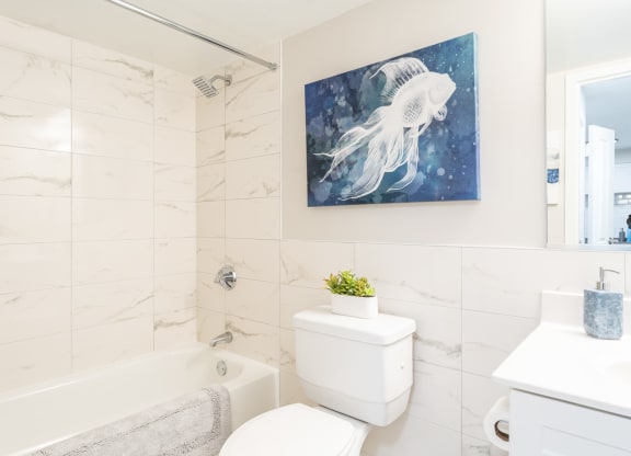 a bathroom with a white tub and toilet and a painting of a white jellyfish