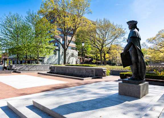A statue of a person stands in a plaza with a building in the background.