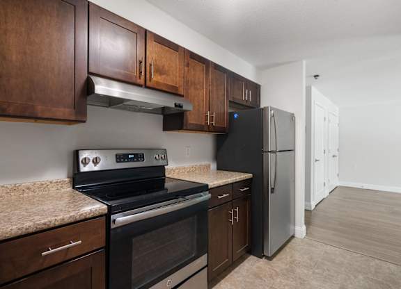 A kitchen with a black stove top oven and a black refrigerator with wooden cabinets.
