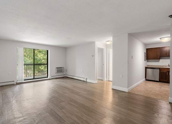 A spacious living room with wooden flooring and a sliding glass door leading to a balcony.