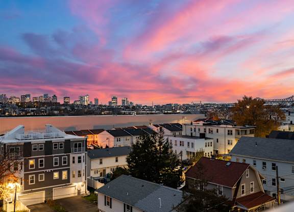 A cityscape at dusk with buildings and a bridge in the distance.