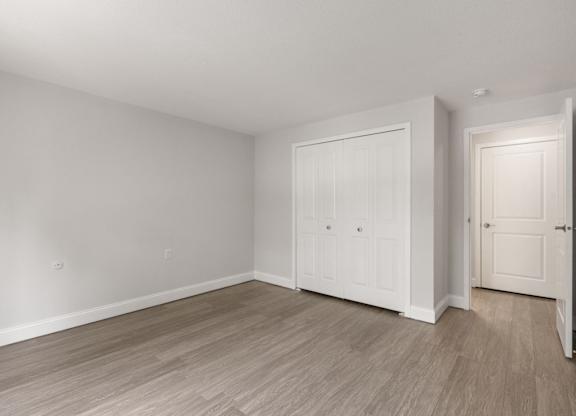 A room with white walls and wood flooring with two doors.