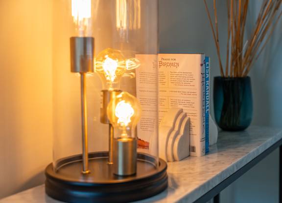 A table with a book, a vase with reeds, and a lamp with a glowing bulb at the Mastlight.