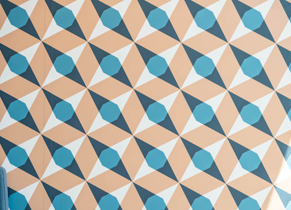 A geometric pattern of blue and peach shapes on a white background A table with a book, a vase with reeds, and a lamp with a glowing bulb at the Mastlight.