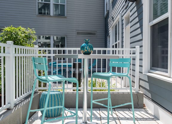 a small patio with blue chairs and a small table with a teal vase on it